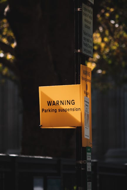 A street view near Westminster Station in London, featuring a large red and blue London Underground sign suspended from a decorative iron lamppost. Beneath the sign, there is a black rectangular direc